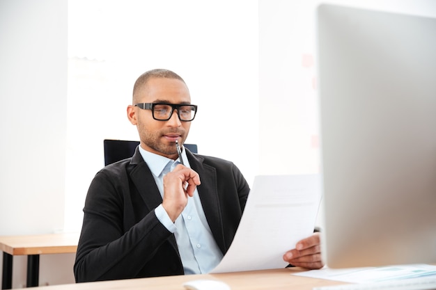A Venezuelan professional working on a laptop, reviewing a credit report with a magnifying glass. The setting is a modern office, emphasizing the importance of financial monitoring.