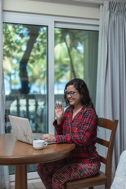 A Venezuelan woman using a laptop to check her credit score online. She is sitting at a table with a cup of coffee and appears focused on the screen. The background shows a modern apartment setting.