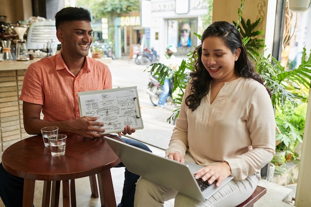 A Venezuelan business owner, wearing a casual shirt, is discussing financial strategies with her management team in a modern office. The scenario captures the brainstorming session, with laptops, digital boards, and stacks of charts representing data analysis and strategic planning.