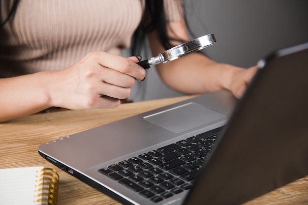A close-up of a hand using a magnifying glass to inspect a suspicious email on a laptop screen, highlighting the need for careful examination and scrutiny.